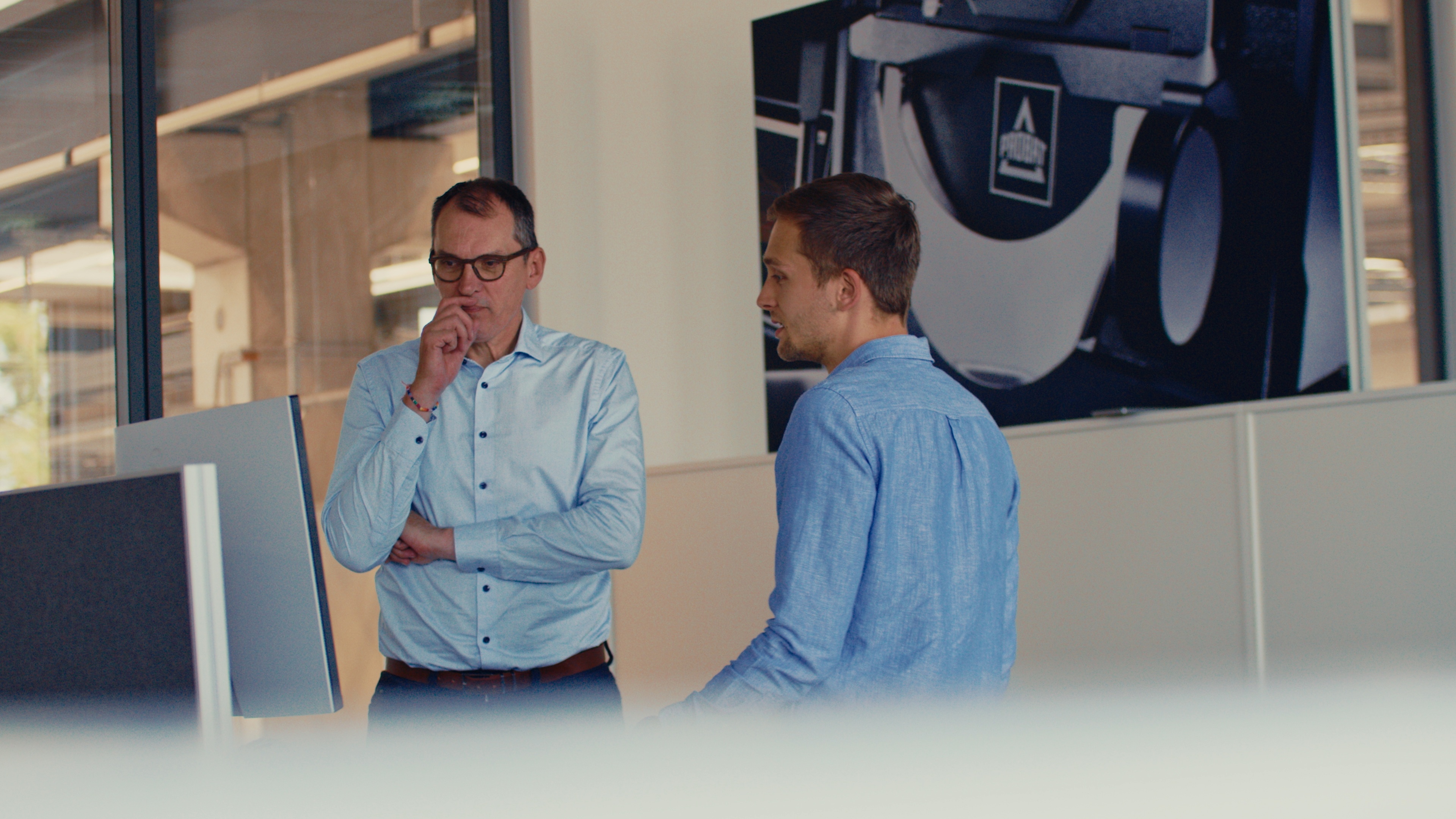 Our CEO Wim in conversation with our employee Noah in front of a desk with computers on it
