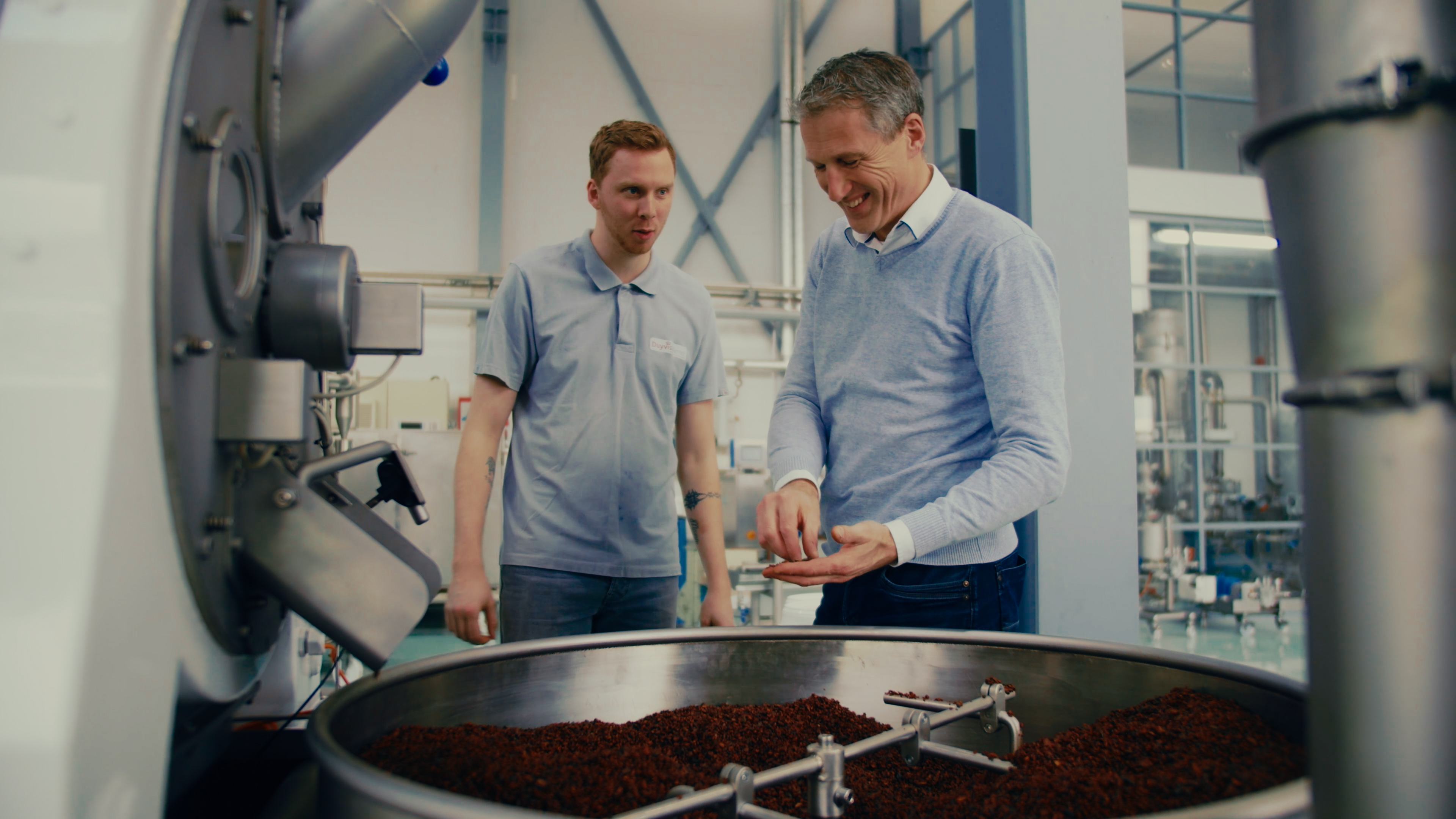 Two employees stand in front of a machine and roast cocoa beans