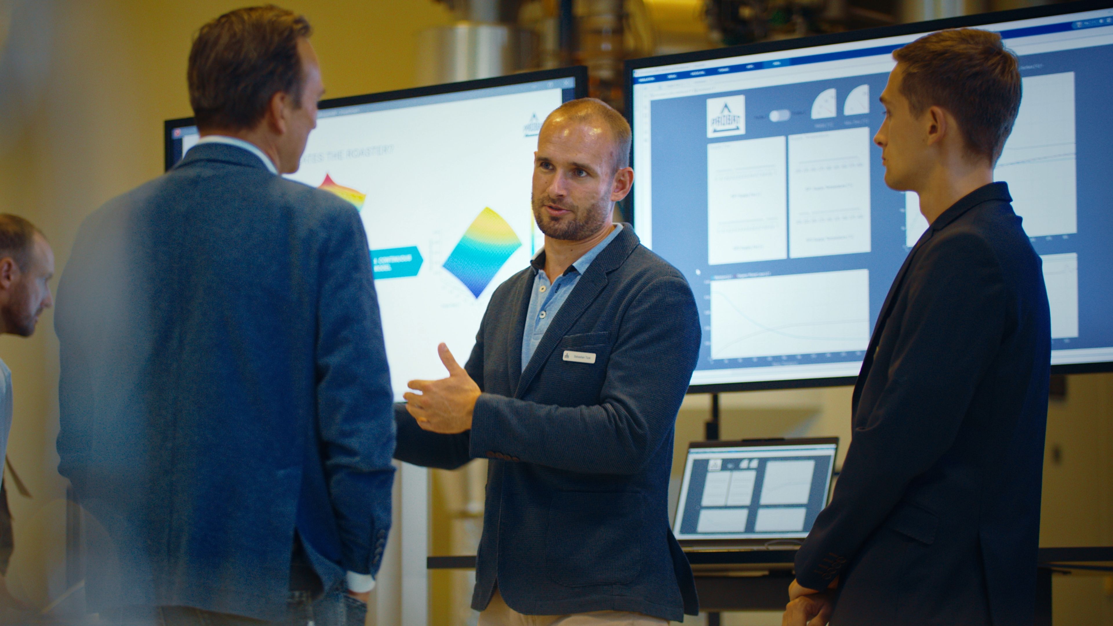 Three men stand in front of screens on which something is being visualized