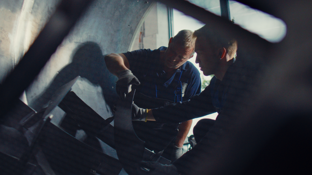 Two men can be seen working on a machine, presumably on a drum inside