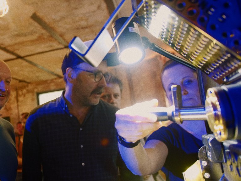 The picture shows two man and Probat employee Daniela in front of a Probat roaster explaining the world of coffee roasting.
