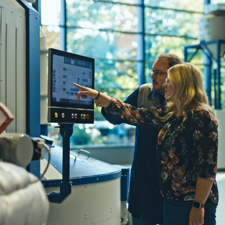 a man and a woman standing in front of a machine at the software control panel