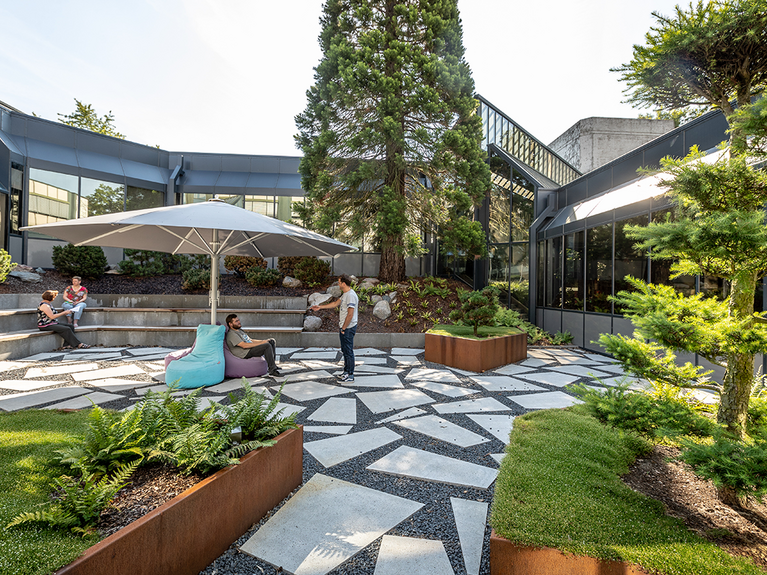 Employees sit on a campus surrounded by the company building and some plants